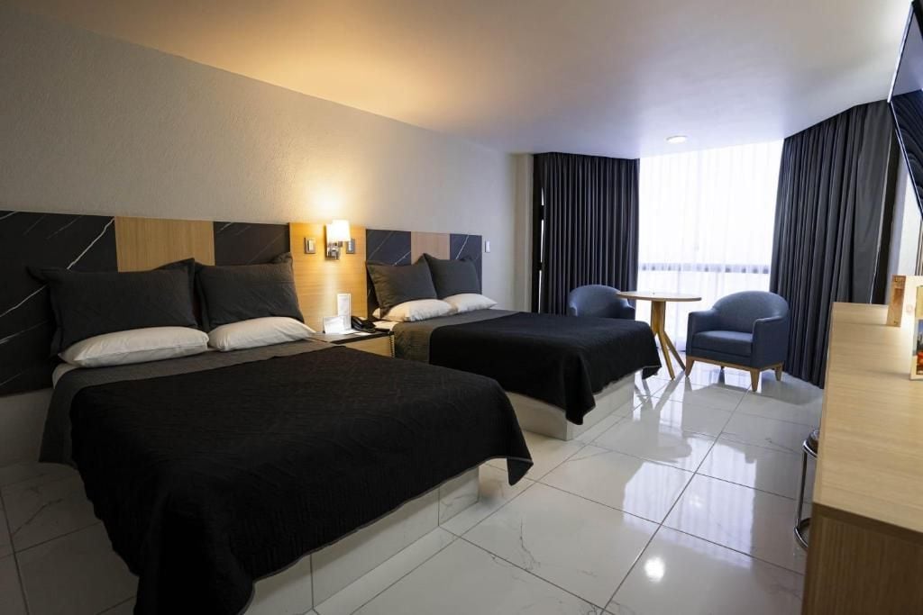 A hotel room with two beds, a desk, a chair, and a window with curtains.
