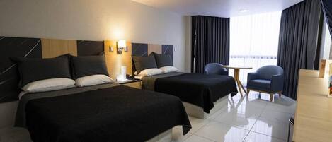 A hotel room with two beds, a desk, a chair, and a window with curtains.