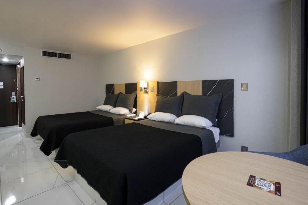 A hotel room with two beds, a small table, and a bathroom with a shower.