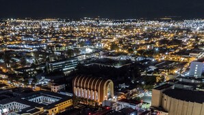 Un edificio alto con varios balcones, rodeado por un paisaje urbano nocturno.