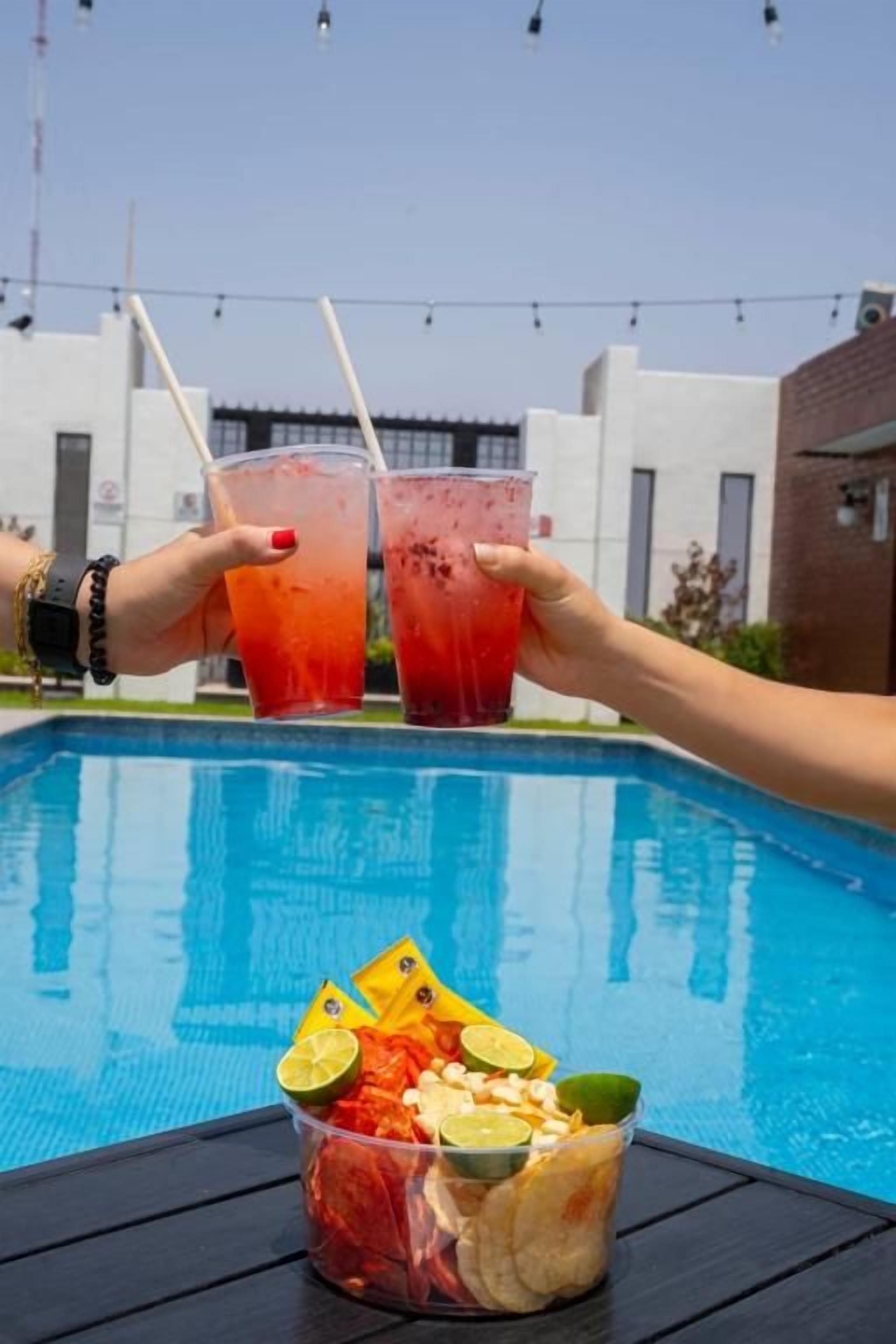 A poolside setting with a clear view of the pool, a table with snacks, and two people toasting with drinks.
