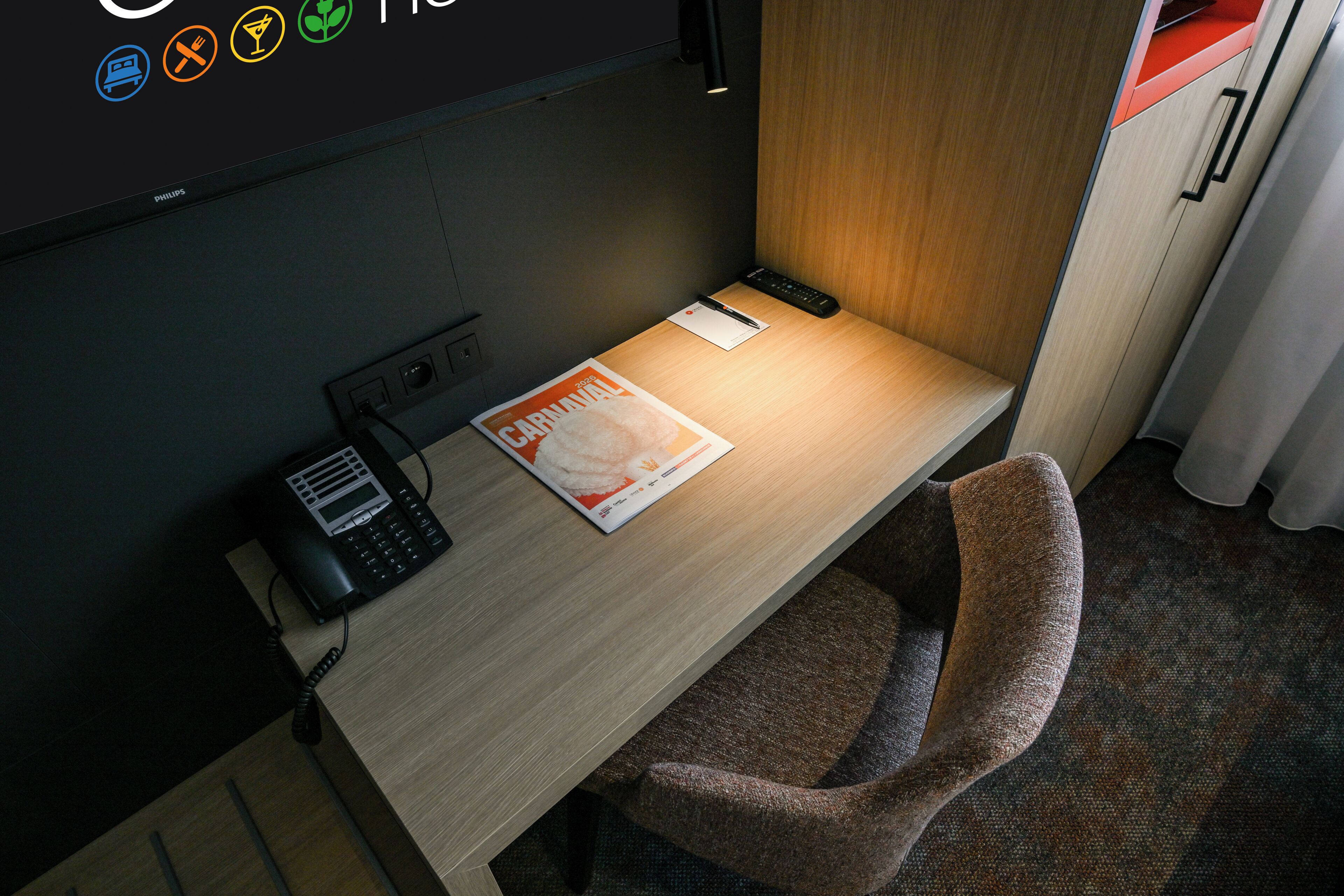 Een hotelkamer met een bureau, telefoon, afstandsbediening en een tijdschrift.