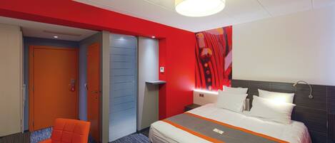A hotel room with a bed, a chair, a door, and a wall with a red and white color scheme.