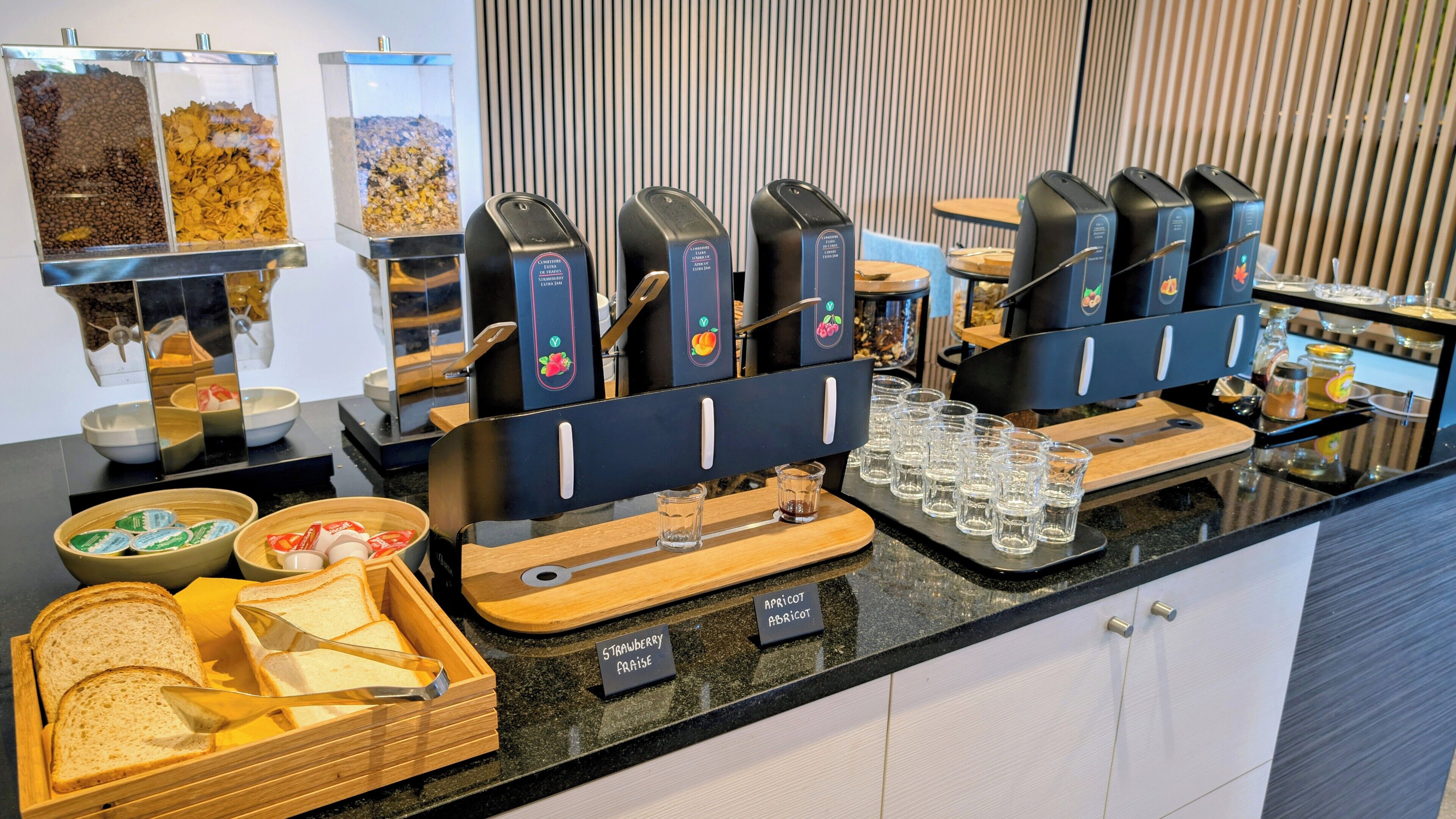 Een buffetopstelling met koffieautomaten, een fruitdispenser en drinkdispensers met aanduiding voor aardbeien- en abrikoosensmaak.