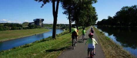 Un sendero pavimentado junto a un canal, con ciclistas y un edificio distante.