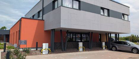 A modern building with a flat roof, large windows, and a parking area.