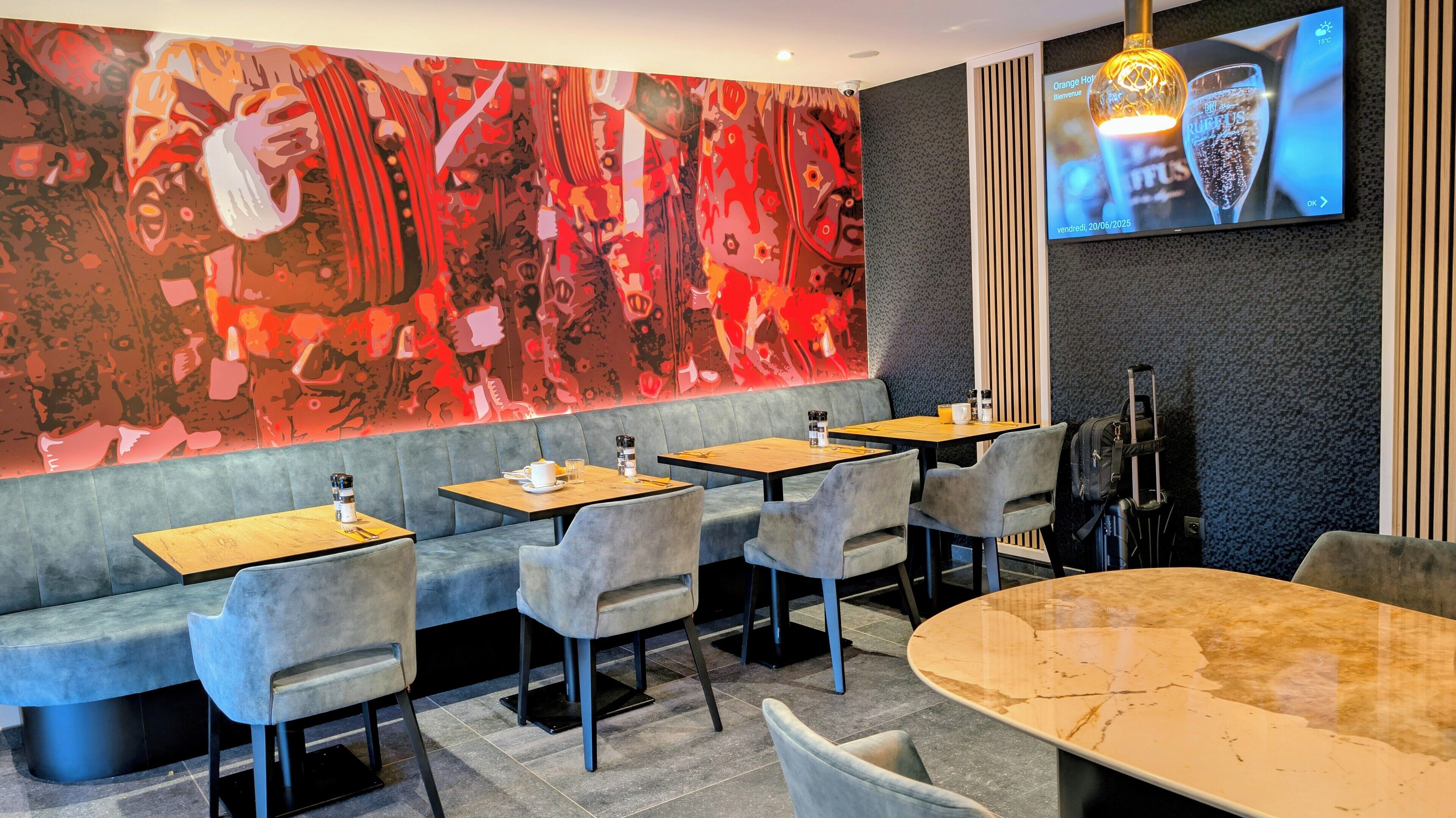Un restaurante moderno con un mural abstracto vibrante, asientos acolchados y una gran pantalla de televisión mostrando un anuncio de bebidas.
