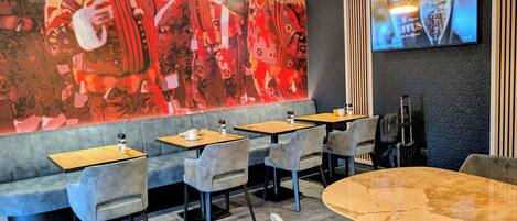 Un restaurante moderno con un mural abstracto vibrante, asientos acolchados y una gran pantalla de televisión mostrando un anuncio de bebidas.