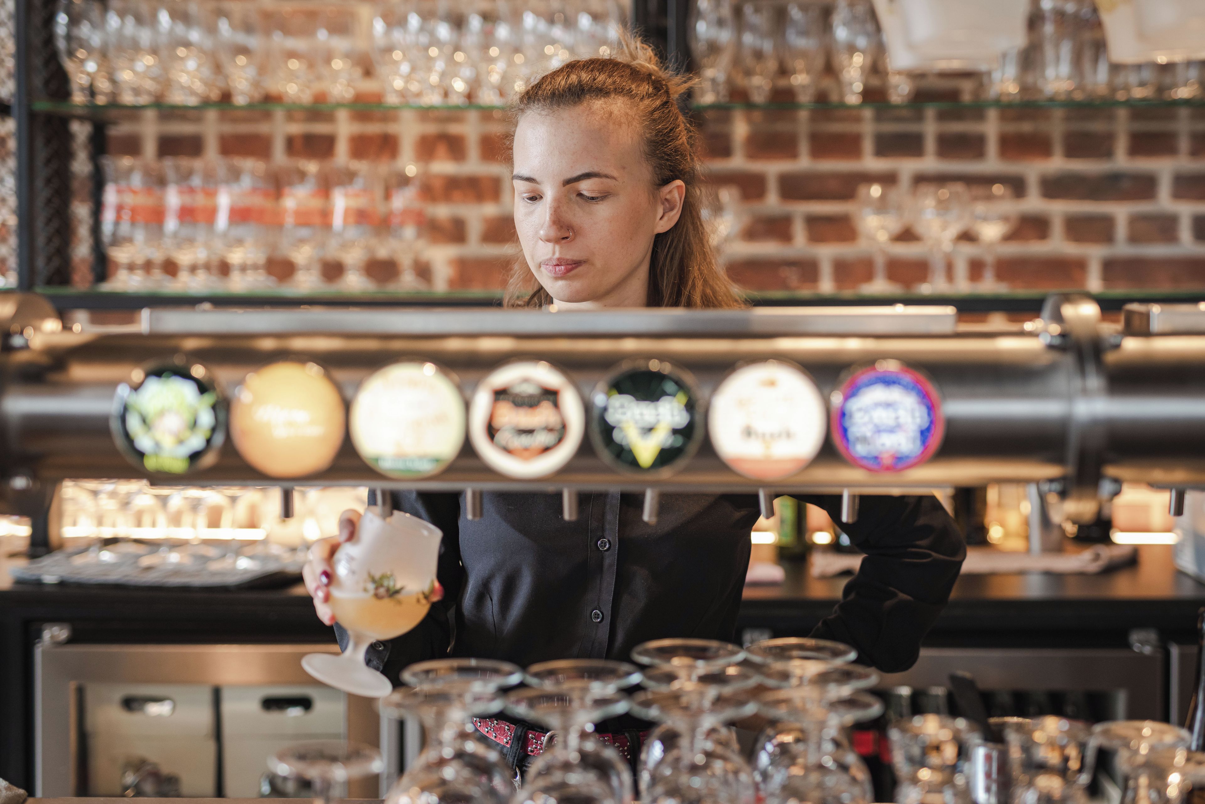 Un barista preparando una bebida detrás de una grifería con diversas opciones de cerveza.