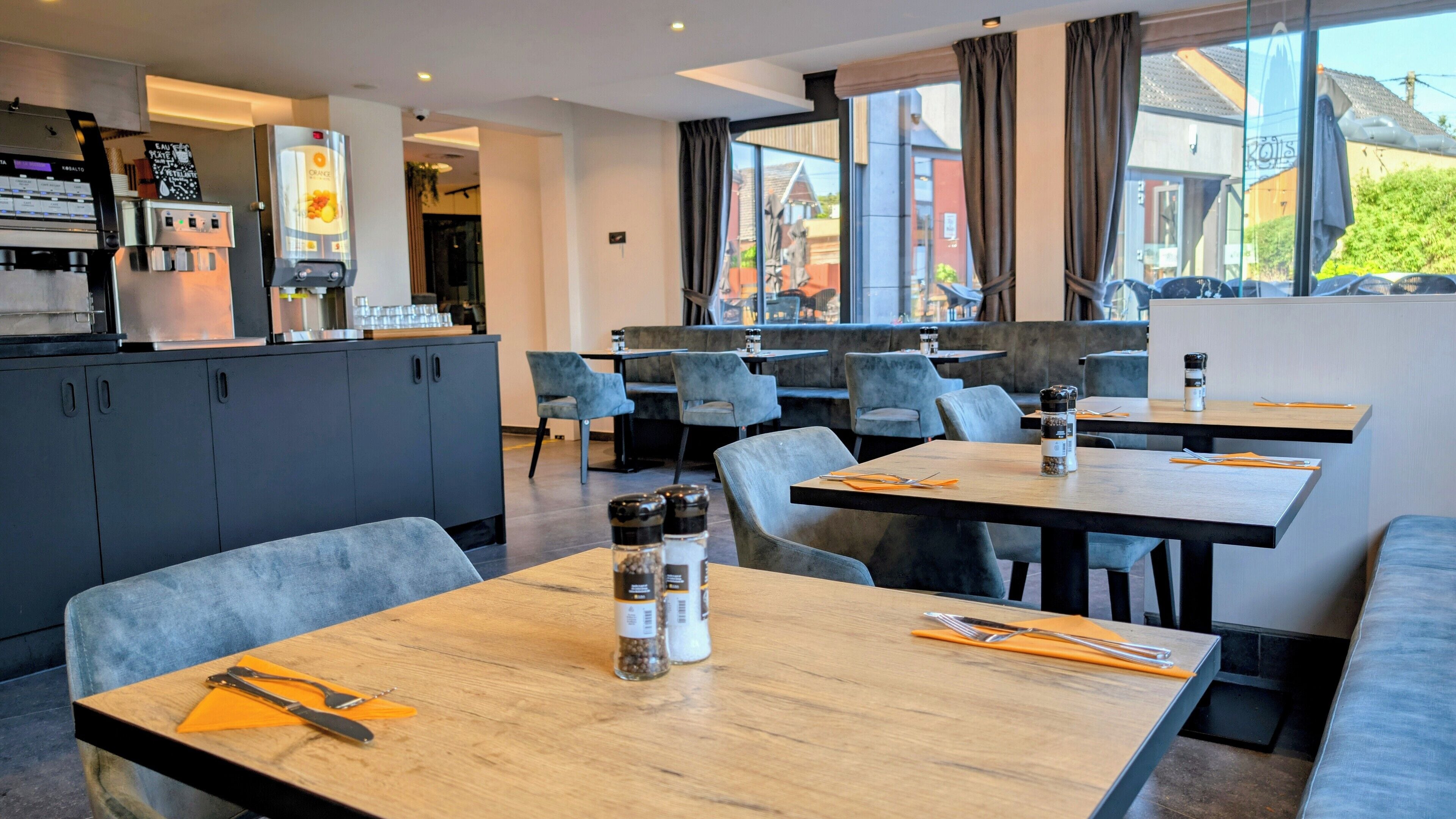 A modern restaurant with wooden tables and grey upholstered chairs.