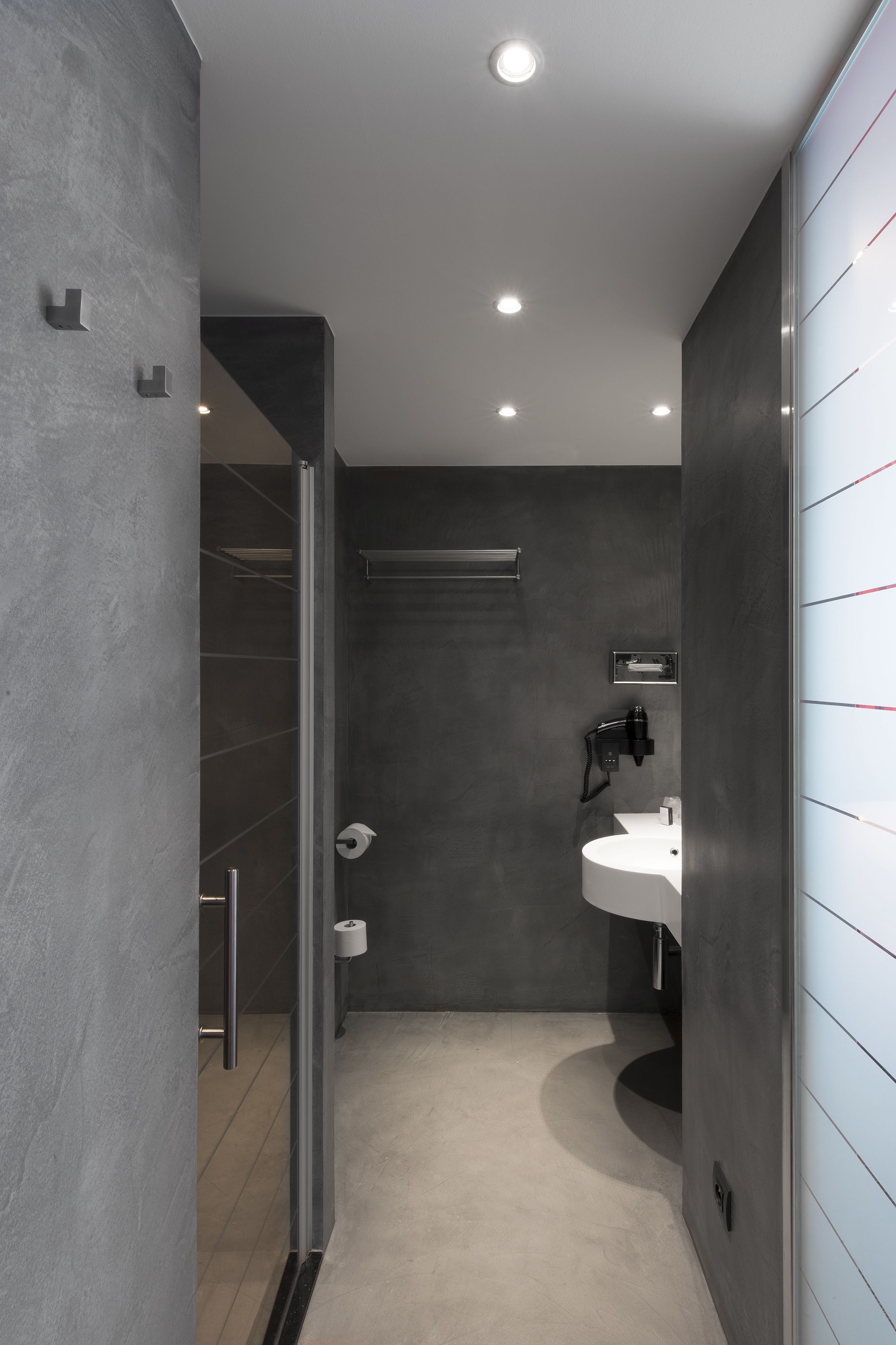 A modern bathroom with a glass shower enclosure, a white sink, and a dark wall.