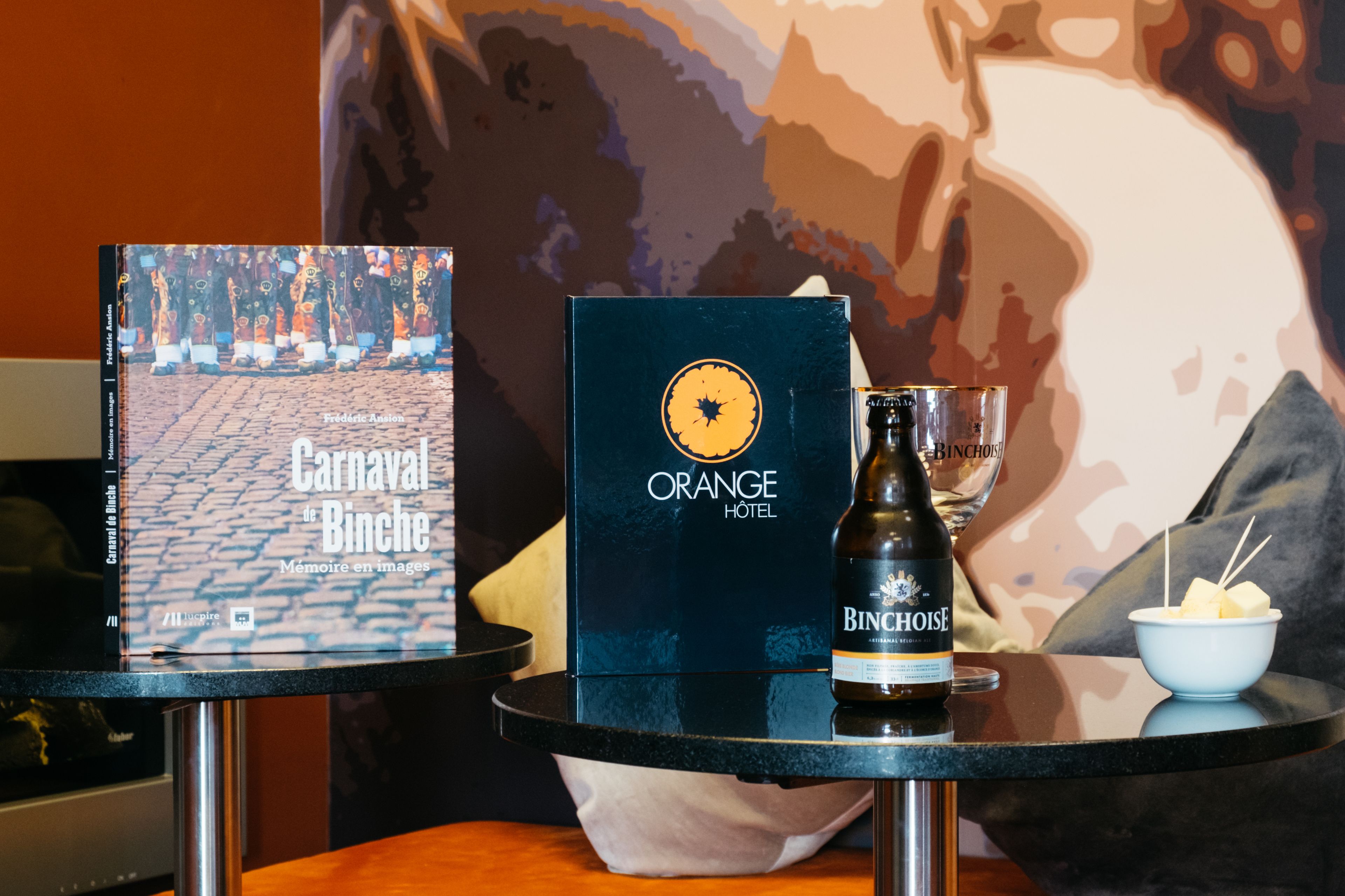 Un livre intitulé « Carnaval de Binche » et une bouteille de vin de Binche sont posés sur une table, à côté d’un verre et d’un bol de fromage.
