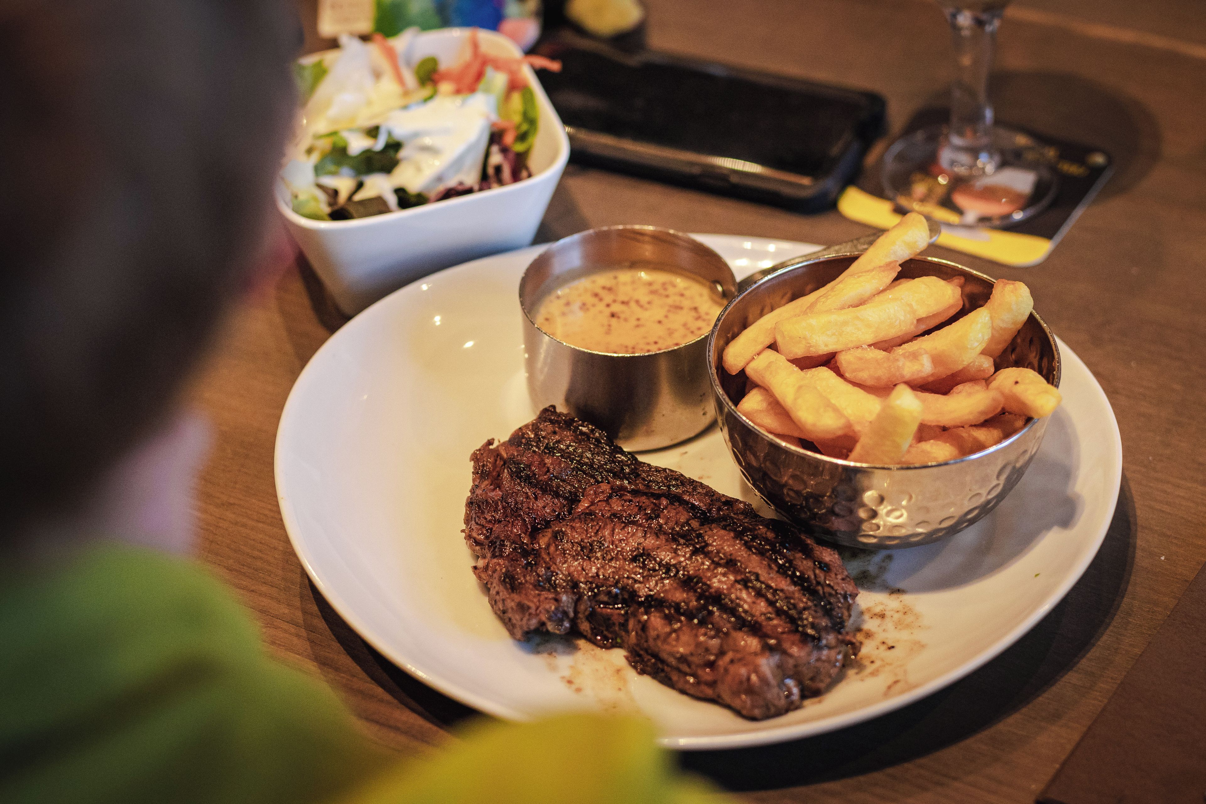 Un plato con un filete, un bol de papas fritas y una taza pequeña de salsa.