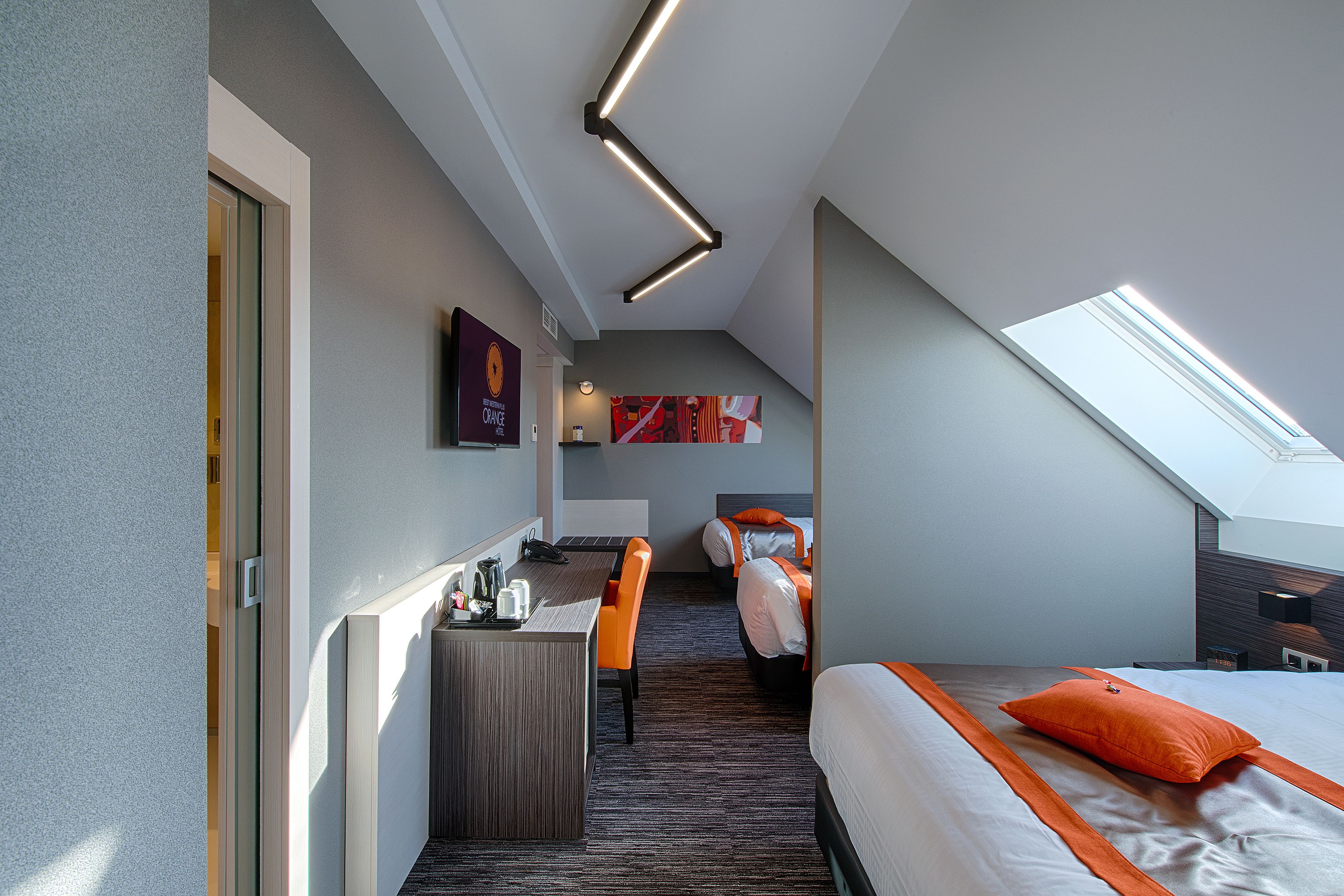A modern hotel room with a desk, two beds, a skylight, and a view of the city.