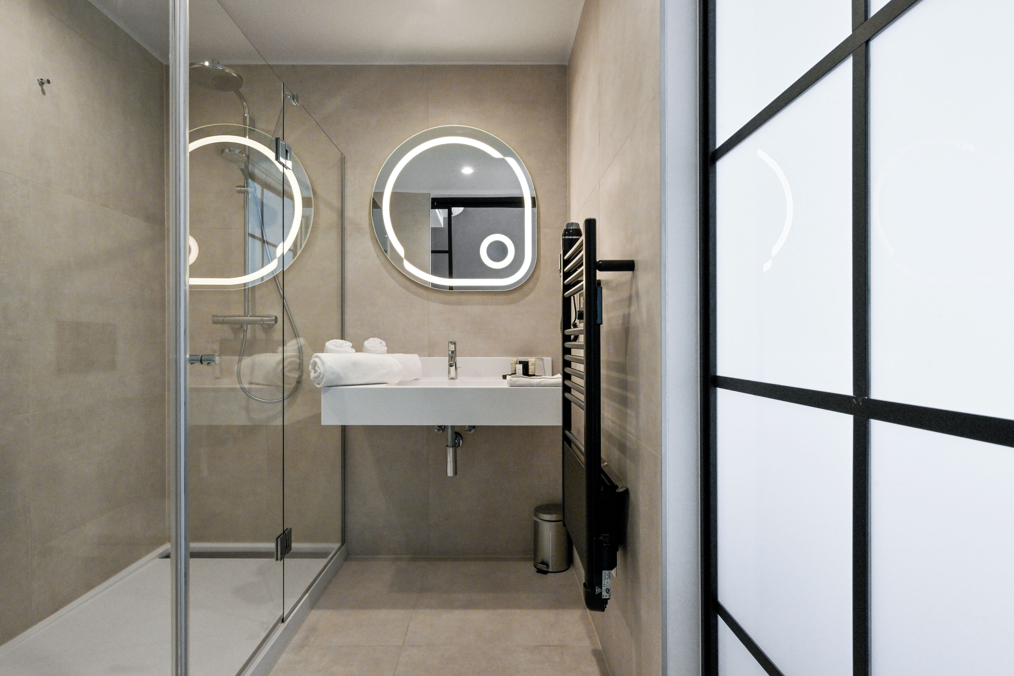 A modern bathroom with a glass-enclosed shower, a sink with a mirror, and a towel rack.