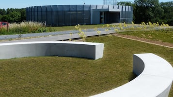 A modern building with a large water tank on the roof, surrounded by a landscaped area with grass and yellow flowers.