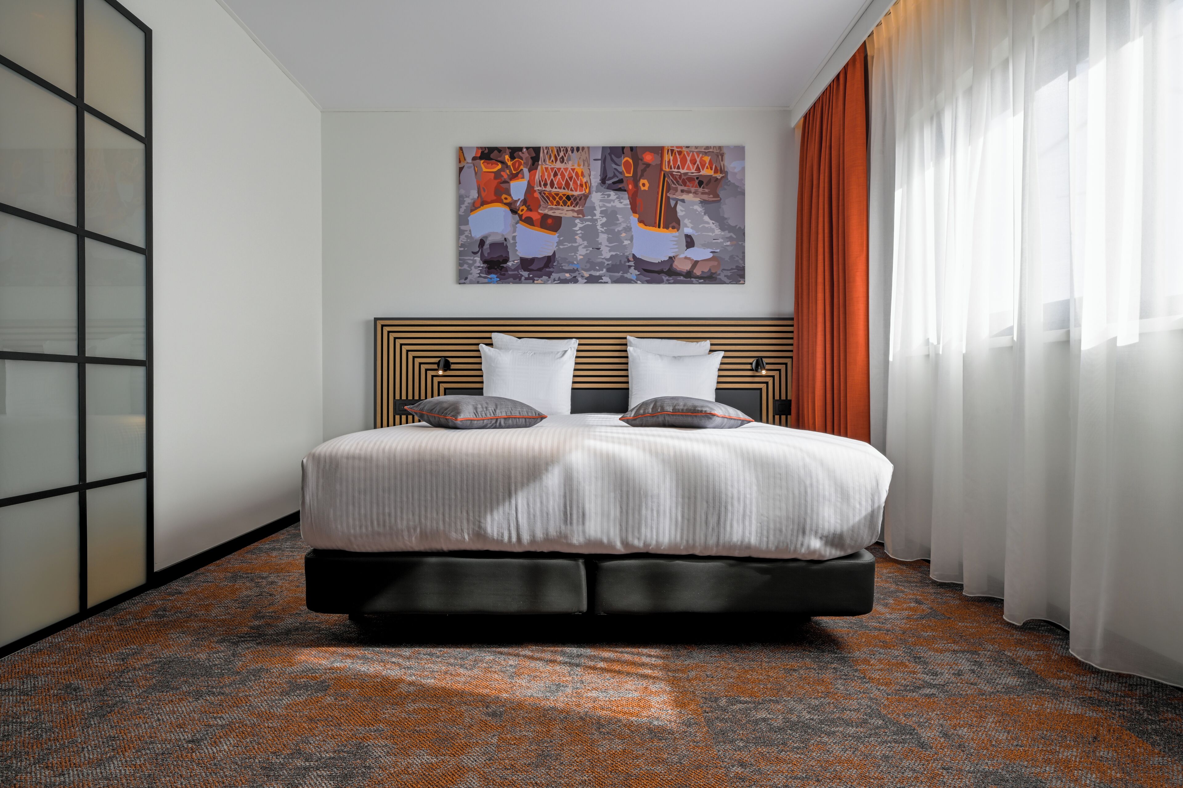 Una habitación de hotel con una cama grande, un cabecero con diseño geométrico, un cuadro sobre la cama y una alfombra estampada.