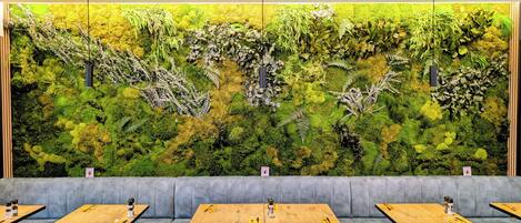 Ein Restaurant mit einer Wandmalerei mit Grün, grauen Sitzkissen und Holztischen.