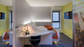 A modern hotel room with a curved desk, a bed with orange pillows, and a view of the city through the window.