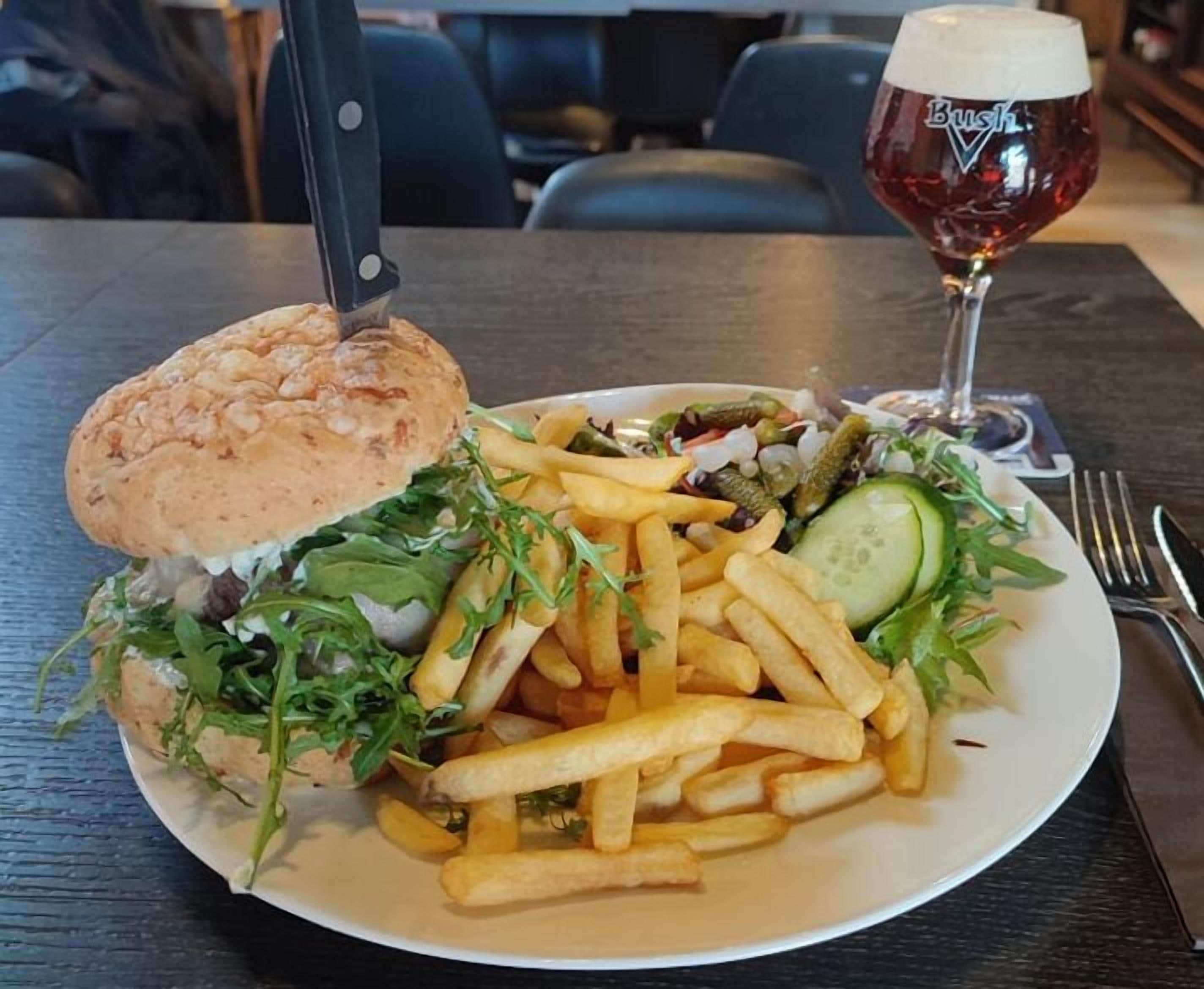 Une assiette avec un hamburger, des frites et une salade, et un verre de bière sur une table.