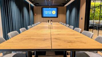 Un salón de conferencias con una larga mesa de madera, sillas tapizadas en gris y una pantalla que muestra el logotipo de Orange Hotel.