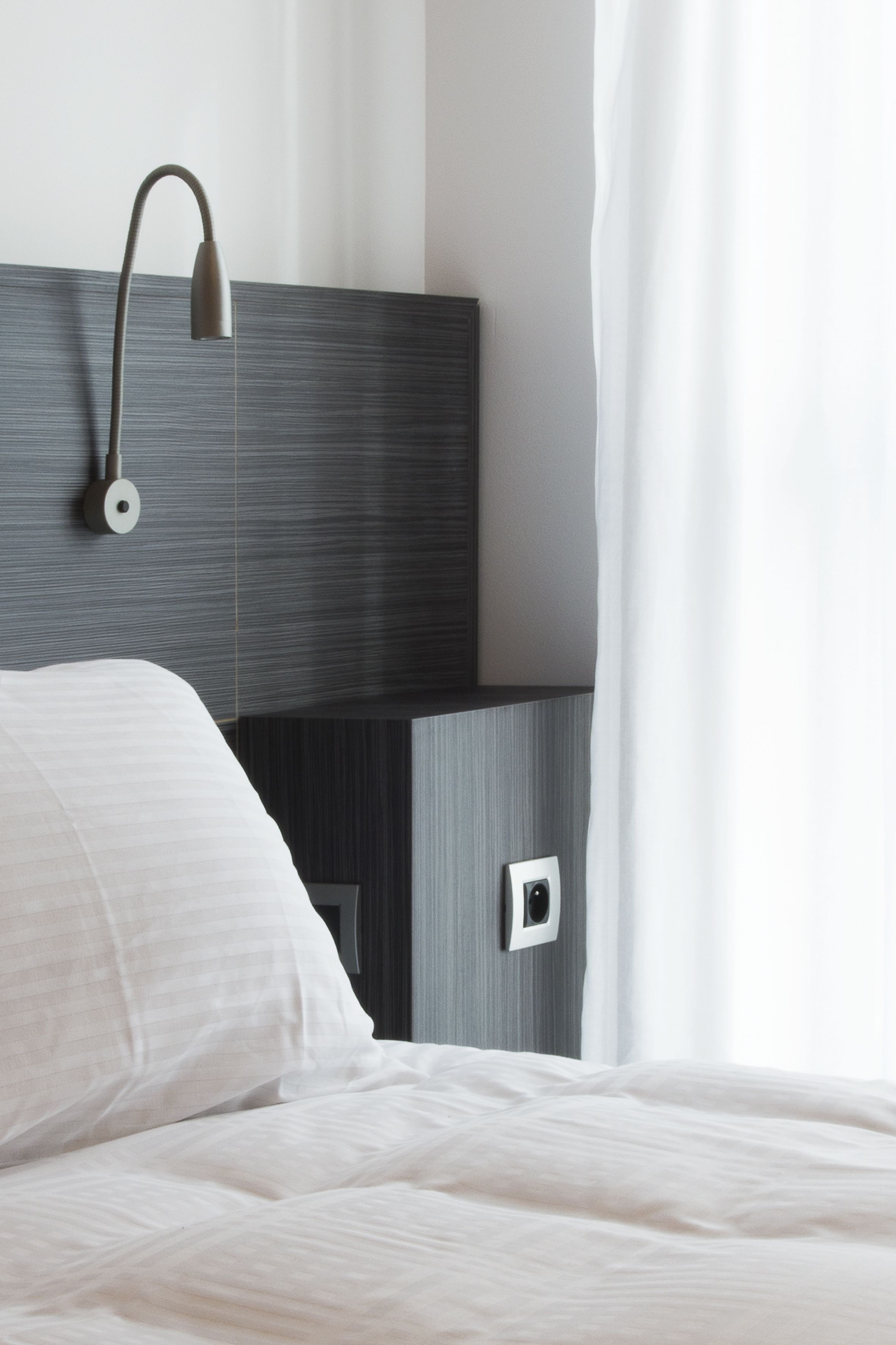 Una camera d'albergo moderna con un letto rifatto, una lampada a parete e un piccolo portafoto.