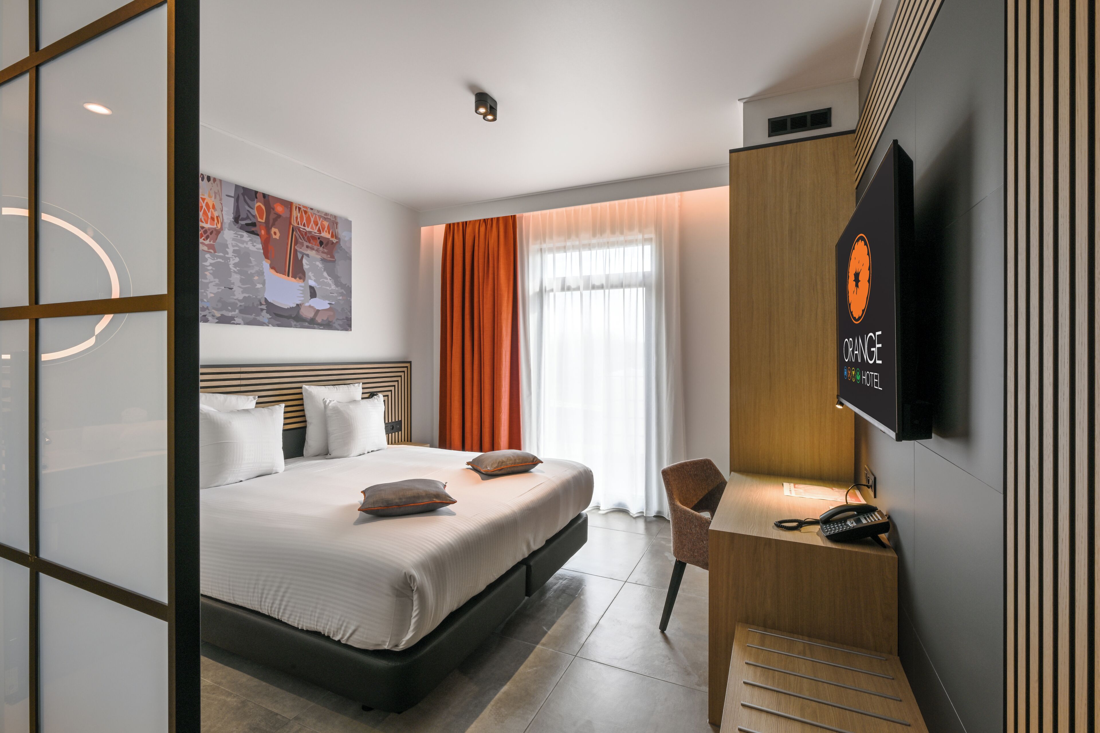 A hotel room with a bed, a desk, a chair, a television, and a painting on the wall.
