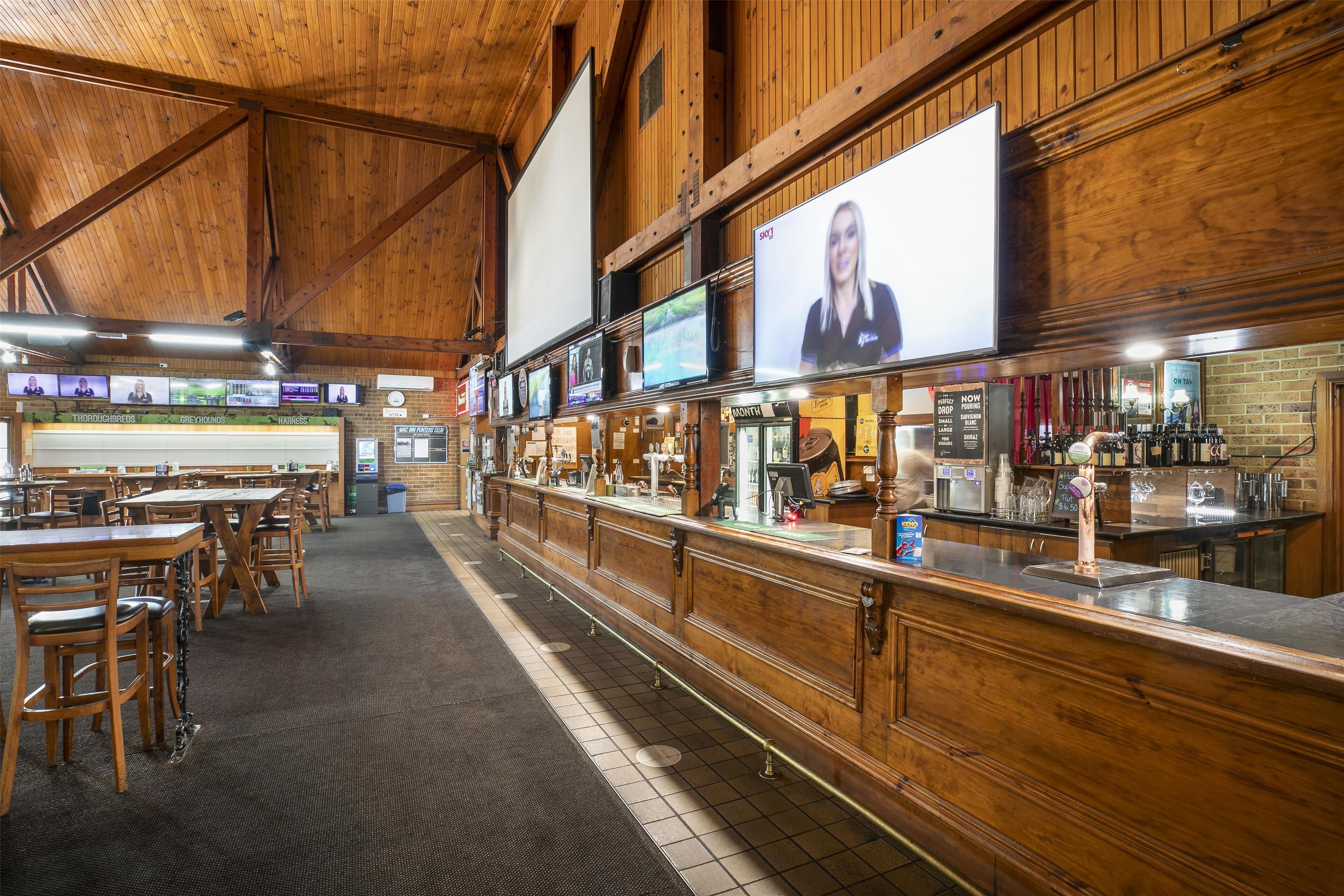 Un grand espace bar doté de comptoirs en bois et de nombreux écrans diffusant différents contenus.