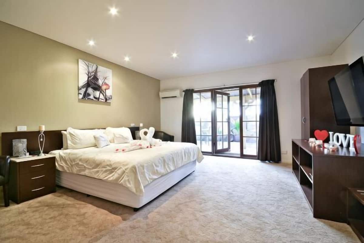 A bedroom with a large bed, a TV, a desk, and a window with curtains.