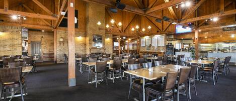 A spacious indoor dining area with high wooden ceilings and brick walls. Tables and chairs are arranged for dining.
