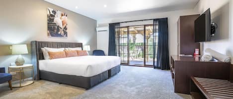 A modern hotel room with a large bed, a desk, a TV, and a balcony with a view.