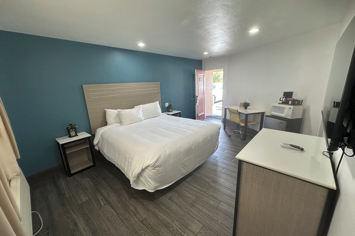A hotel room with a bed, bedside tables, a desk, a chair, a microwave, and a television.