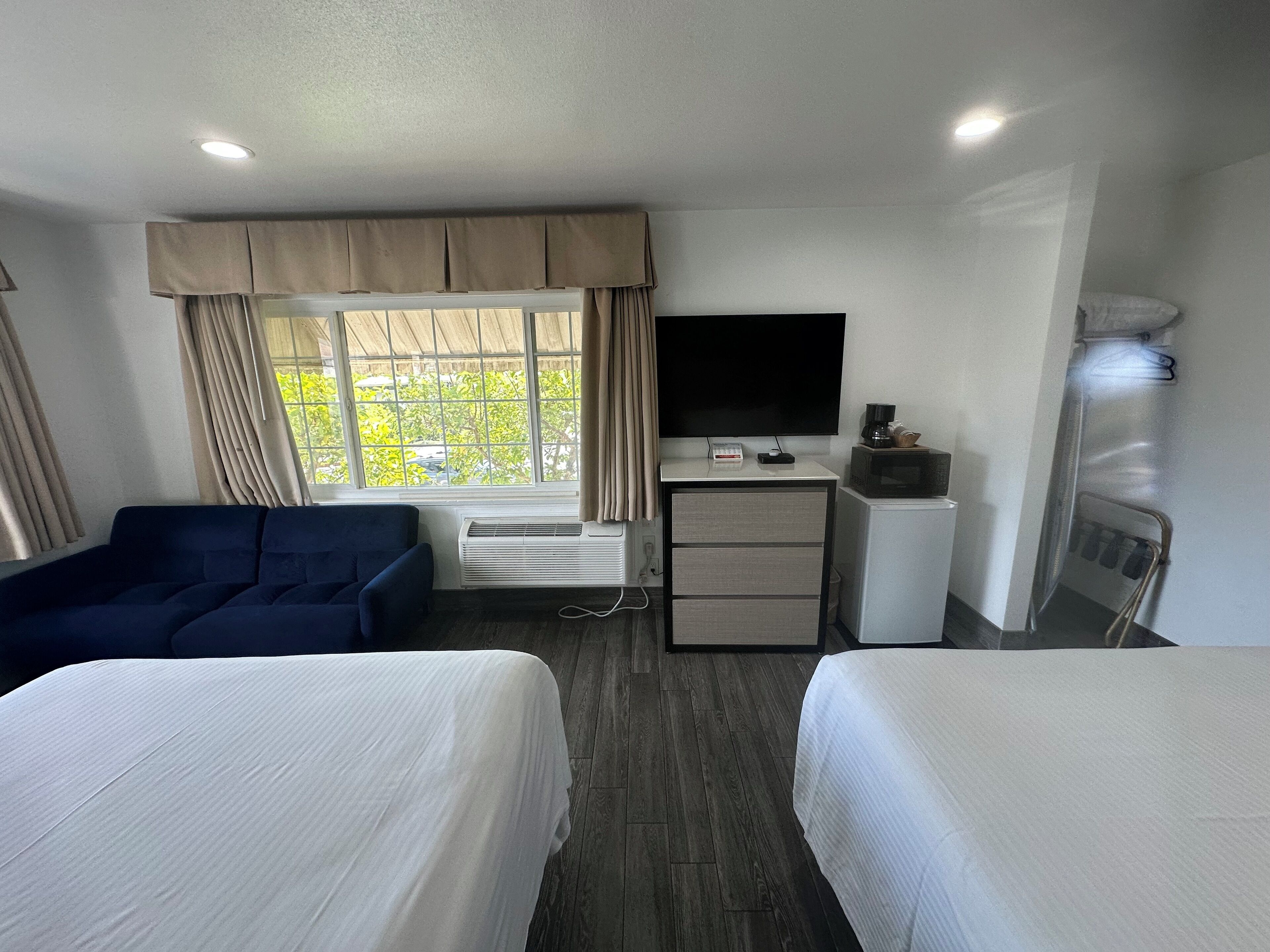 Habitación de hotel con dos camas, un sofá, un escritorio con televisor, un microondas y una ventana con cortinas.