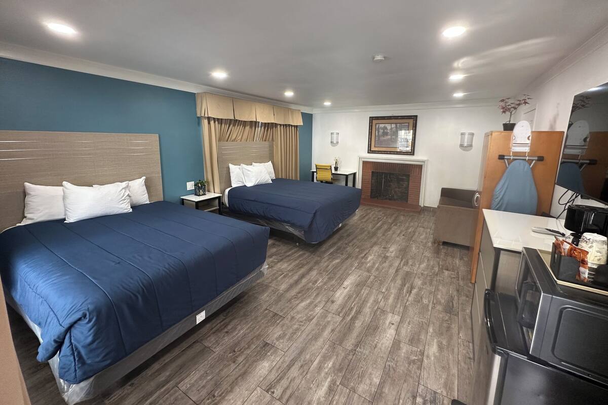 A hotel room with two beds, a small table, a chair, a fireplace, and a desk with a computer.