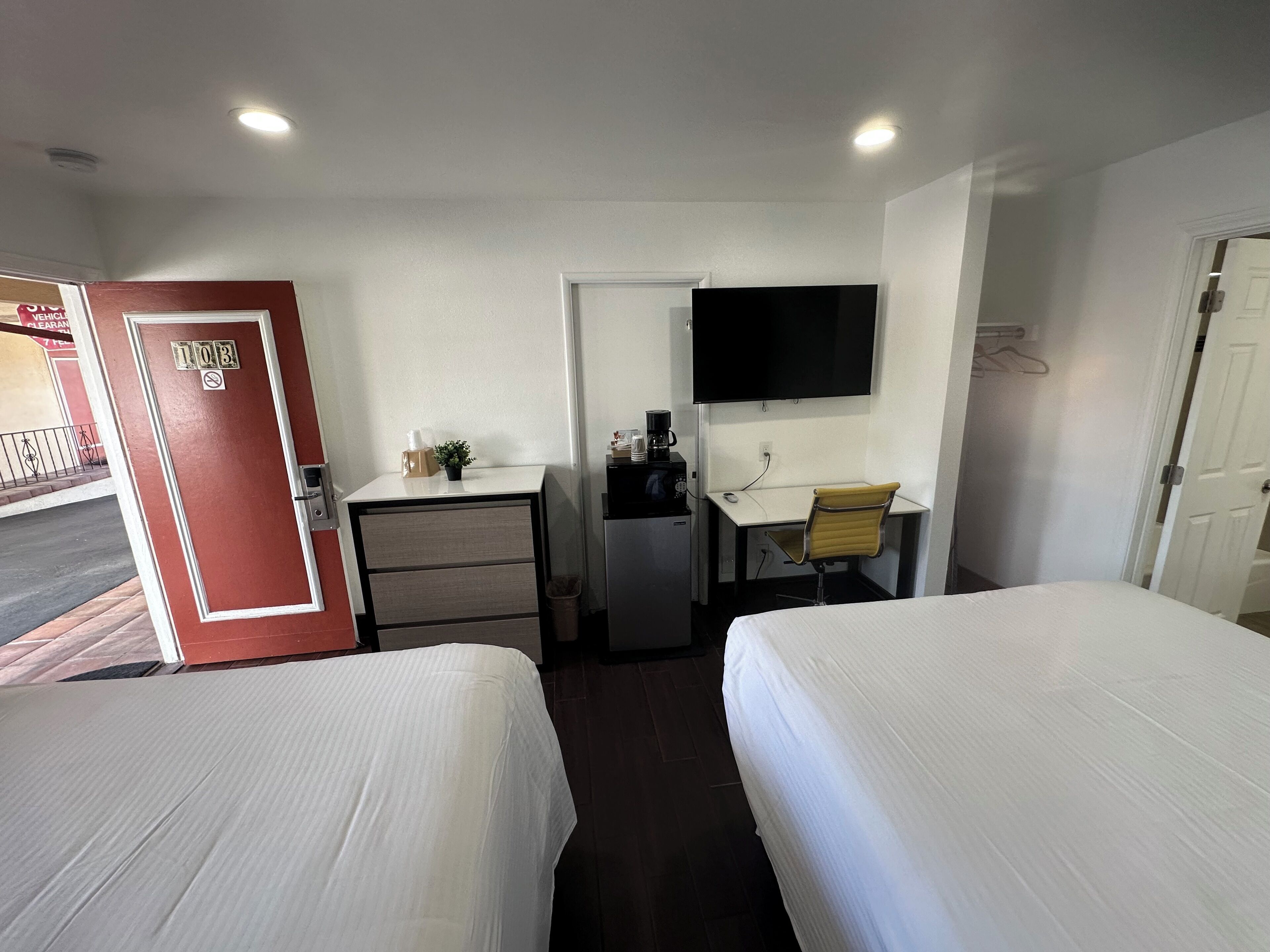 A hotel room with two beds, a desk with a chair, a TV, and a small kitchenette.