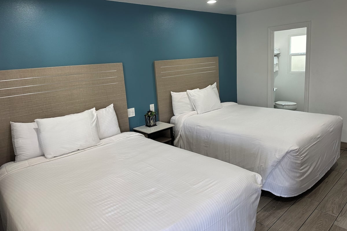 A hotel room with two beds, a nightstand, and a bathroom visible through an open door.
