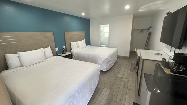 A hotel room with two beds, a TV, a coffee machine, and a shower area.