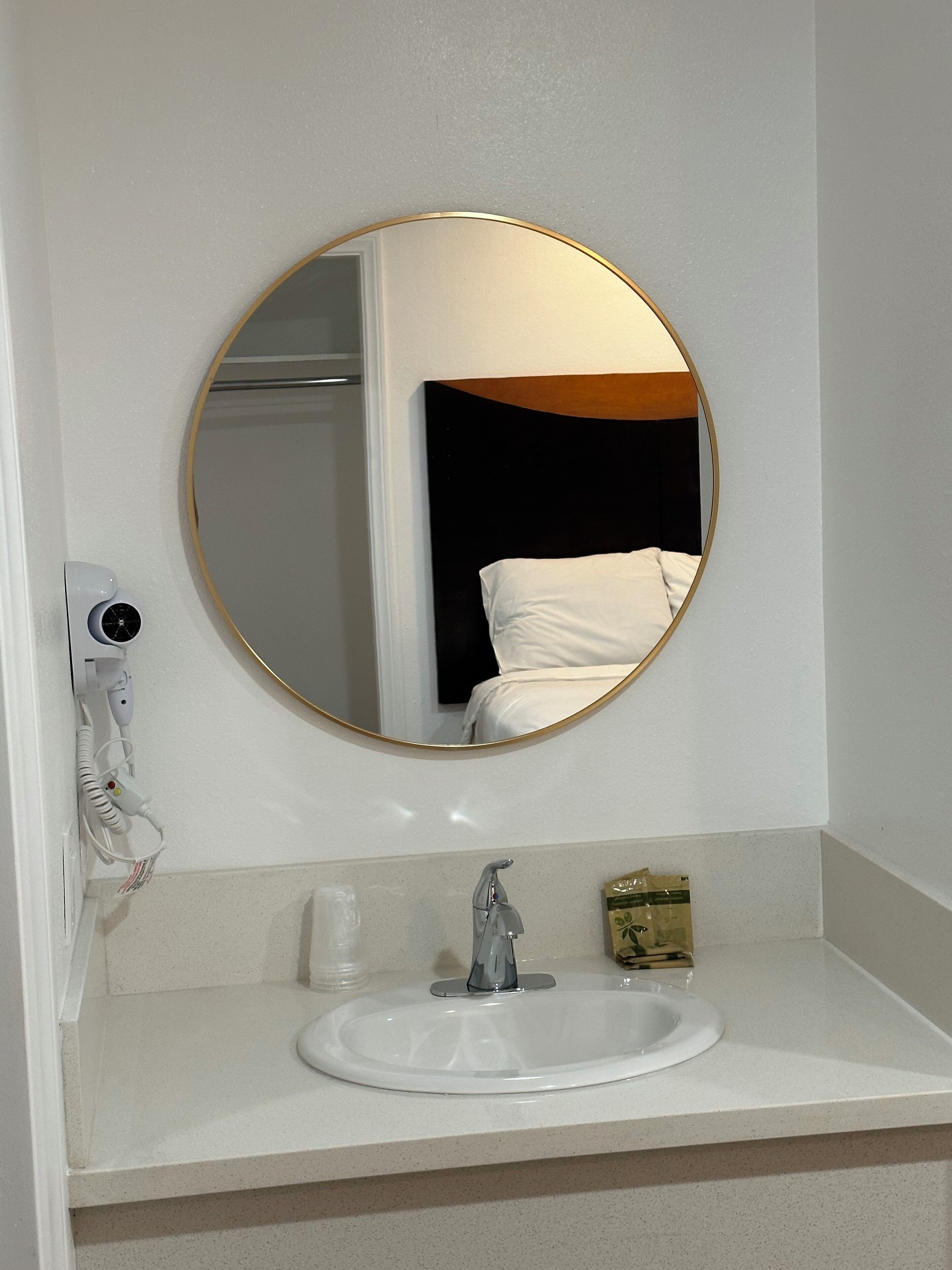 A bathroom with a round mirror, a sink, and a hairdryer on the wall.