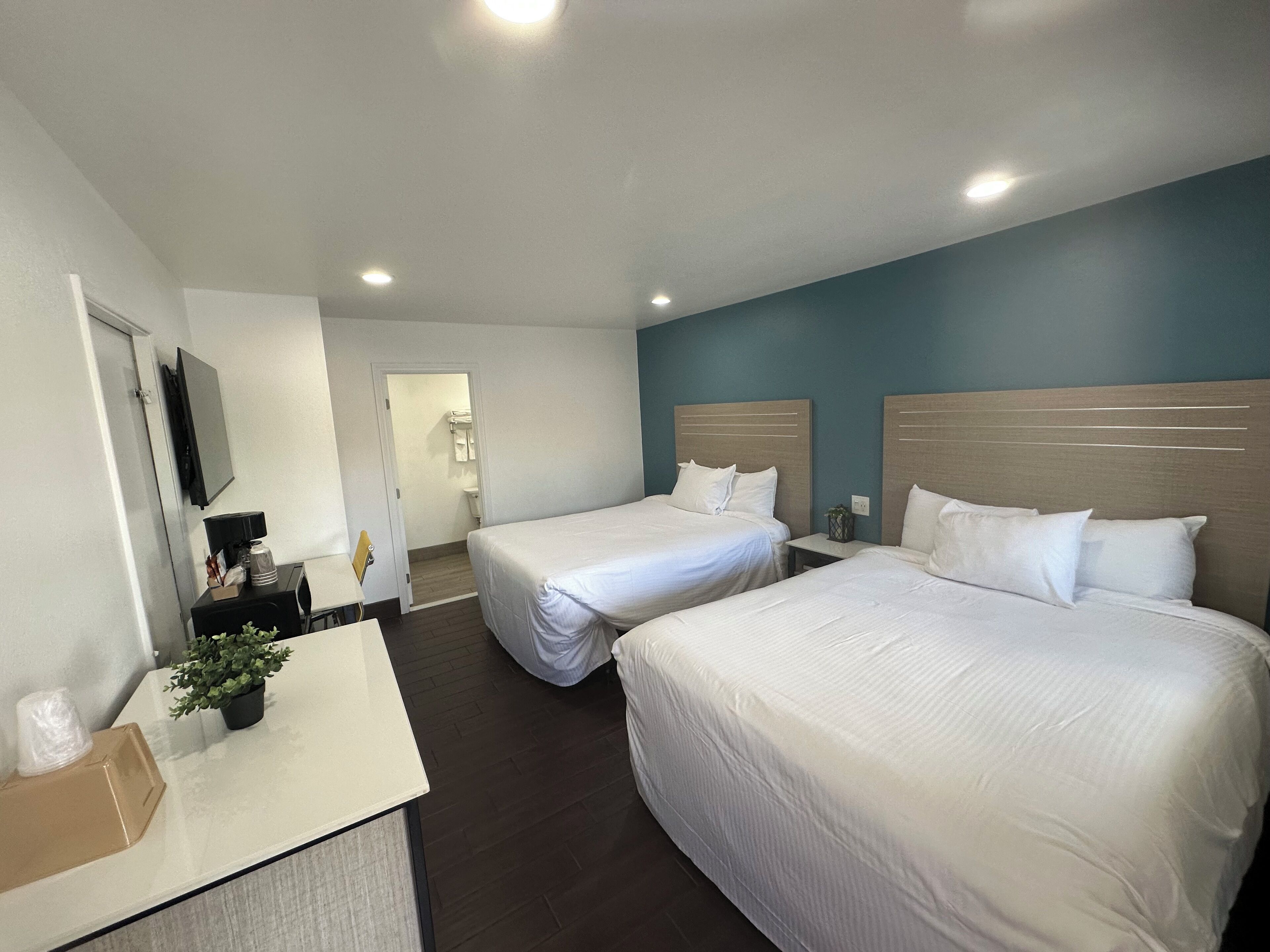 A hotel room with two beds, a desk, a mirror, and a bathroom visible through an open door.