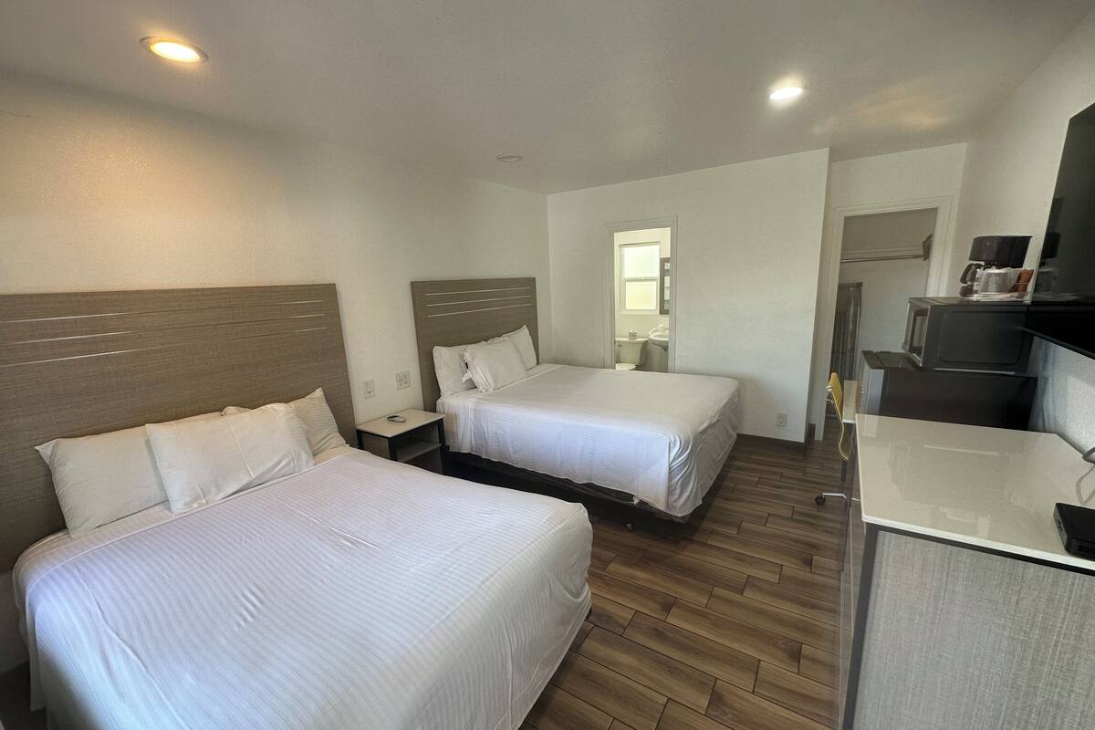 A hotel room with two beds, a small desk, a microwave, and a bathroom visible through an open door.