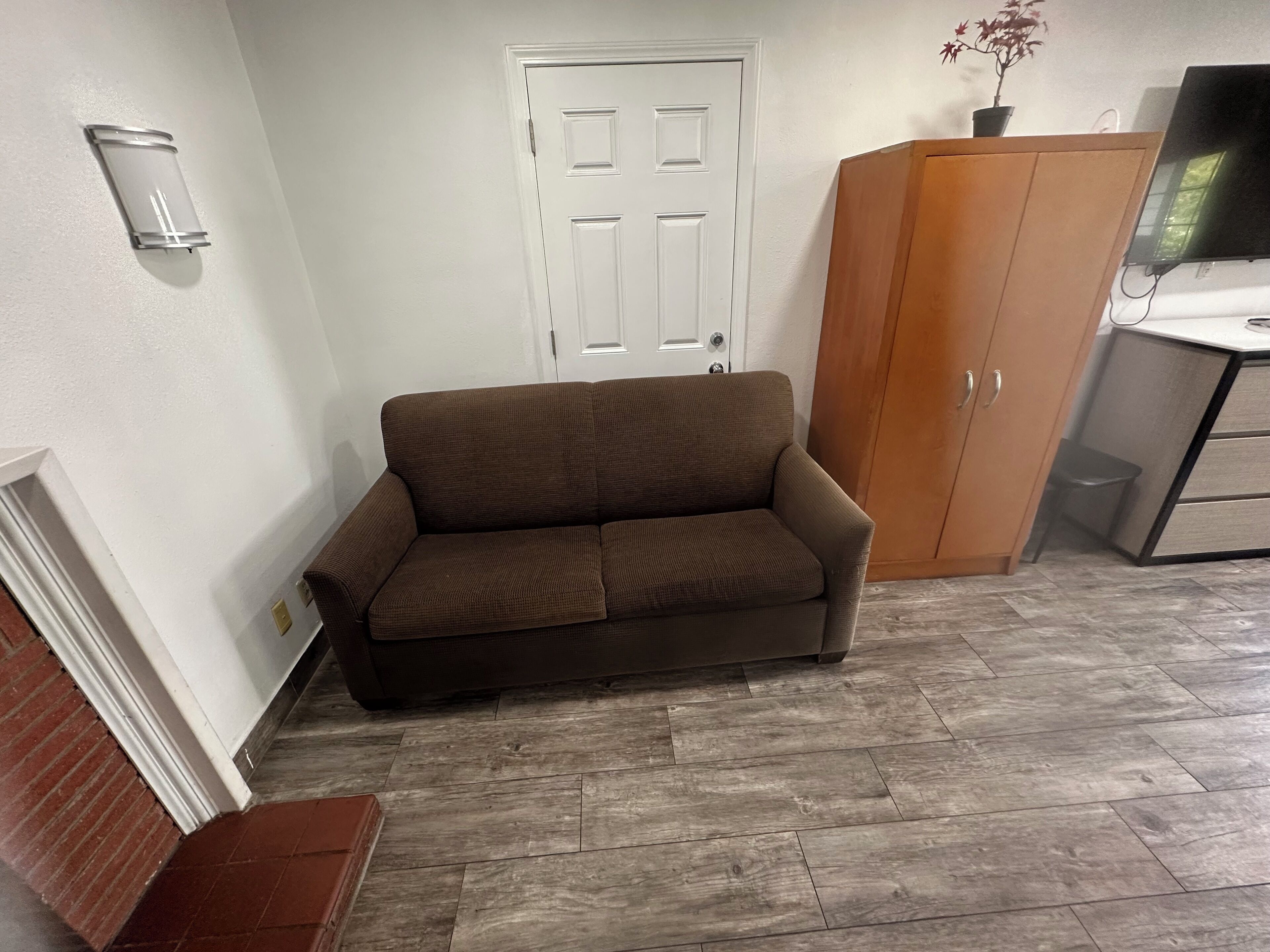 A room with a brown sofa, a white door, a wooden cabinet, and a television on a stand.