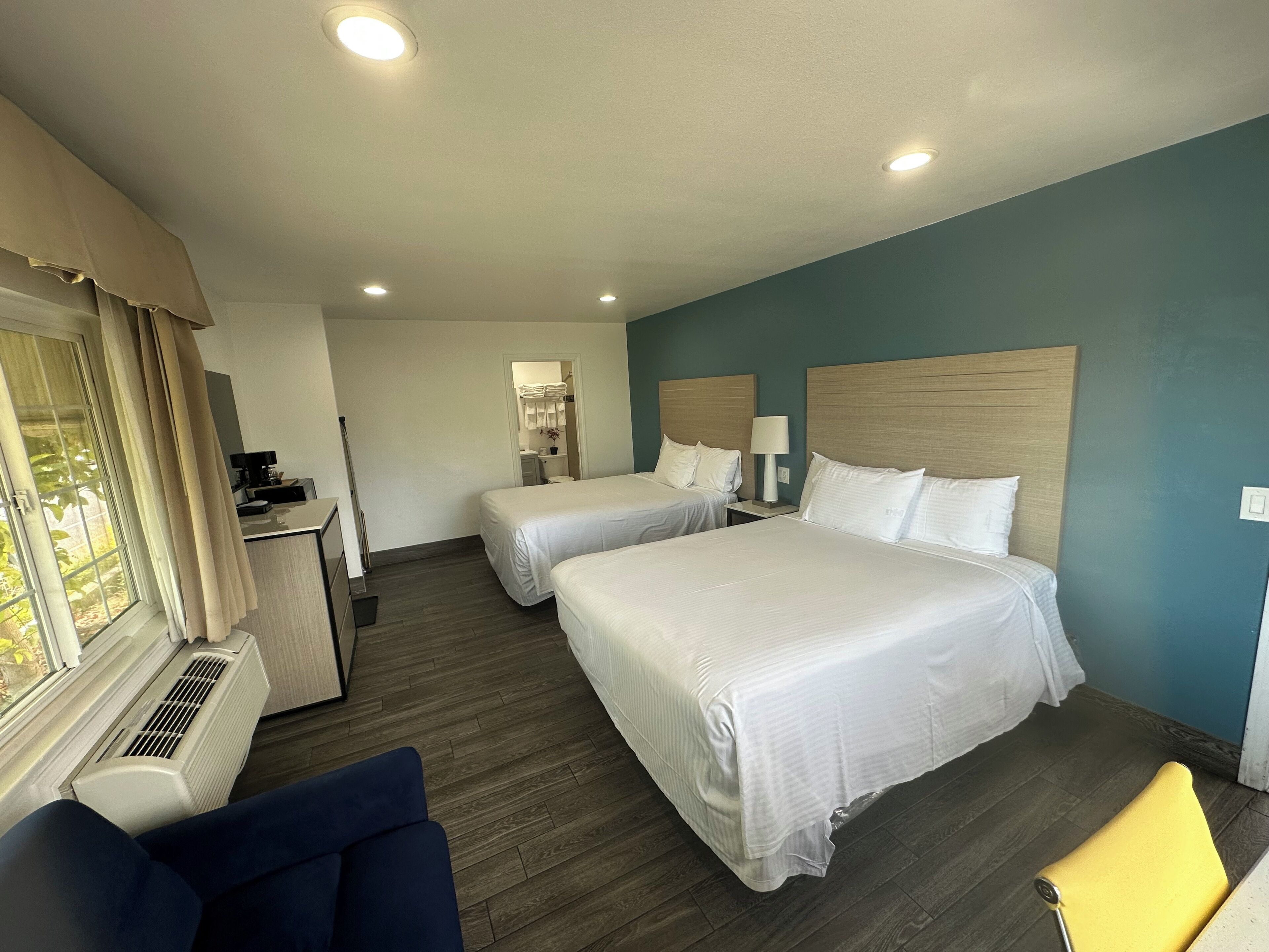 A hotel room with two beds, a desk, a chair, and a window with curtains.