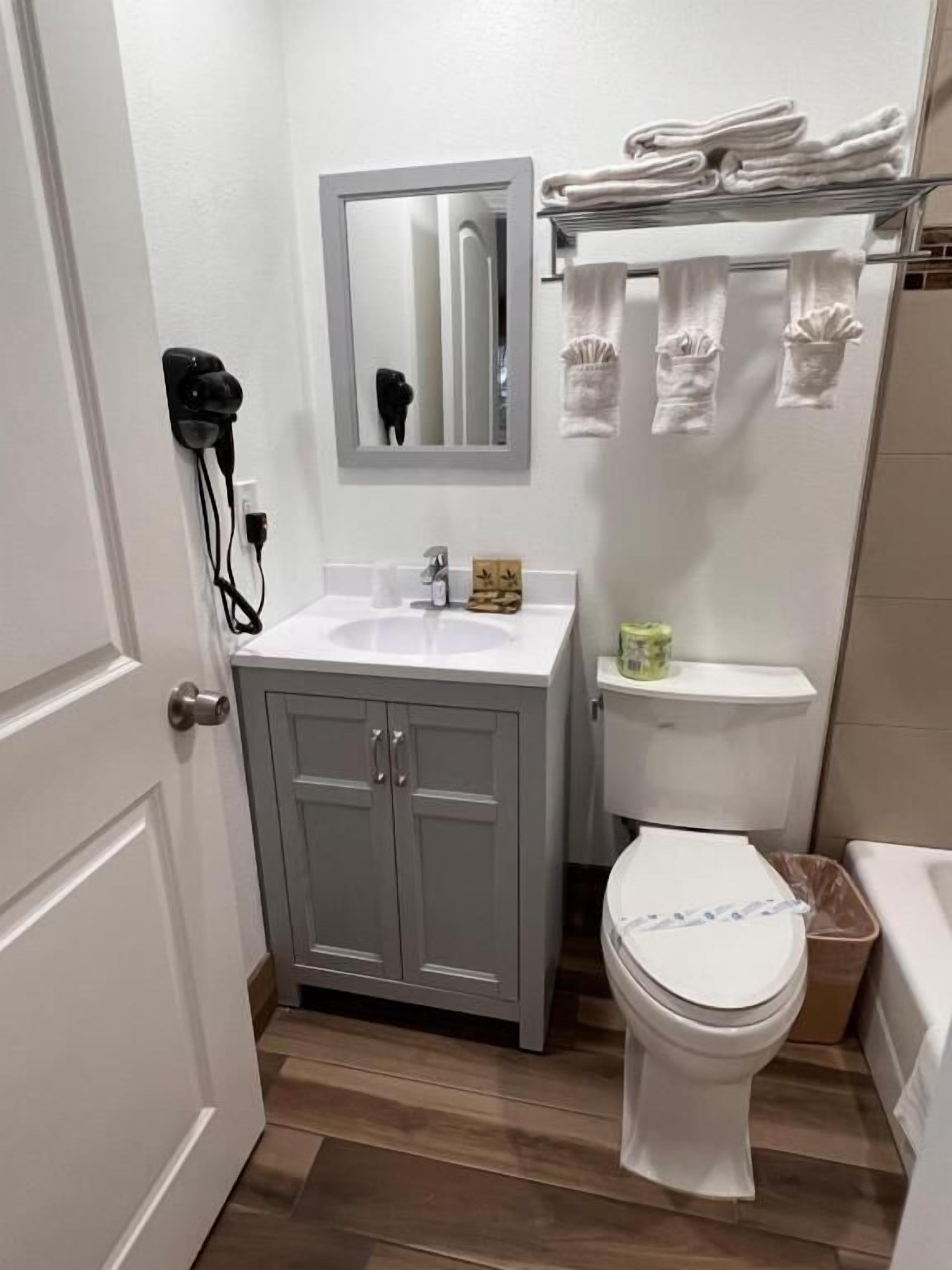 Une petite salle de bain avec un lavabo blanc, des toilettes et un miroir au-dessus du lavabo. On y trouve un porte-serviettes avec des serviettes pliées et une petite étagère contenant des articles de toilette.