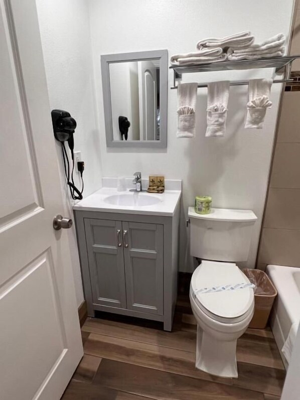 A compact bathroom with a white sink, a toilet, and a mirror above the sink. There is a towel rack with folded towels and a small shelf with toiletries.