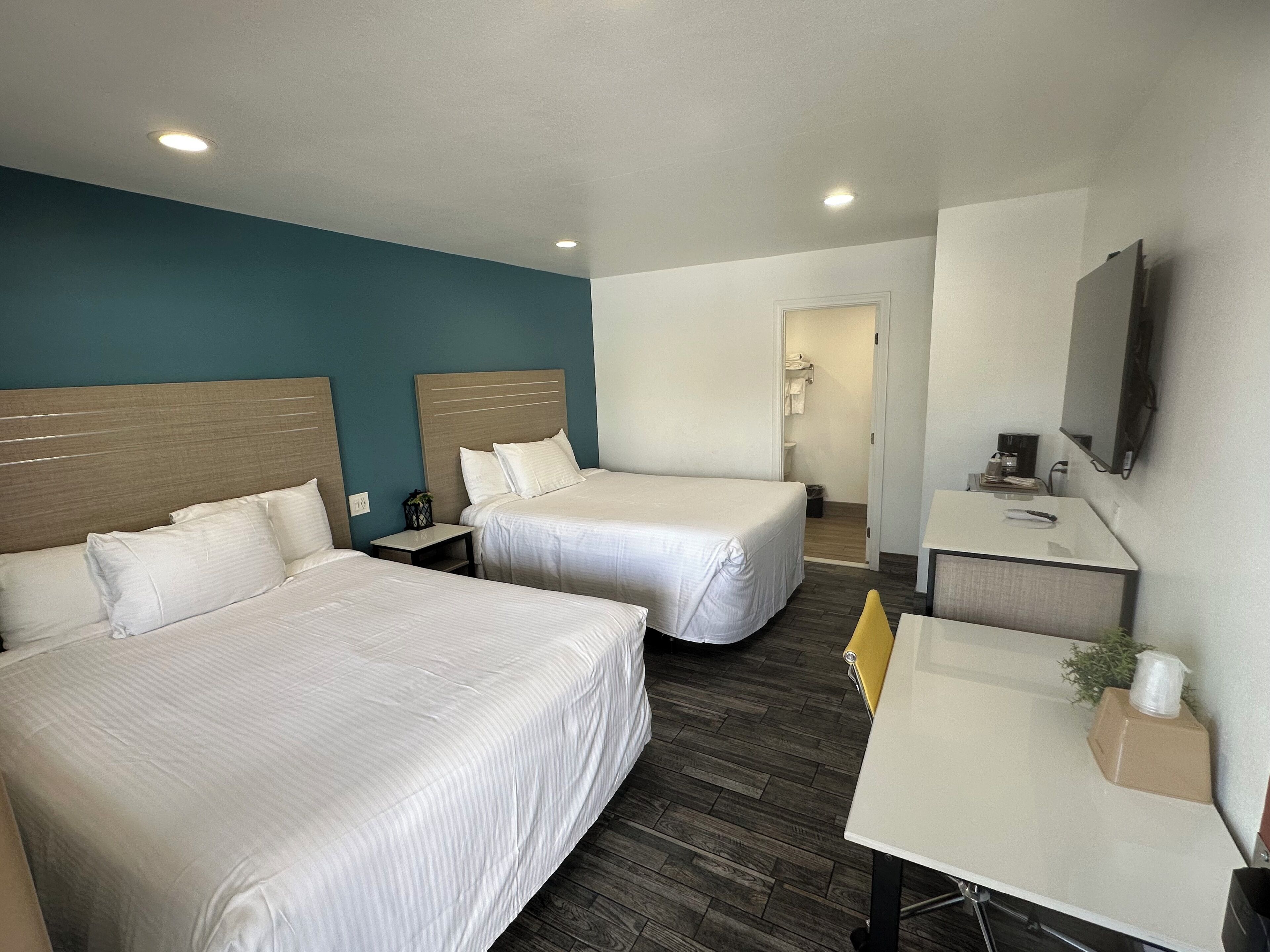 A hotel room with two beds, a desk, a chair, a TV, and a bathroom visible through an open door.