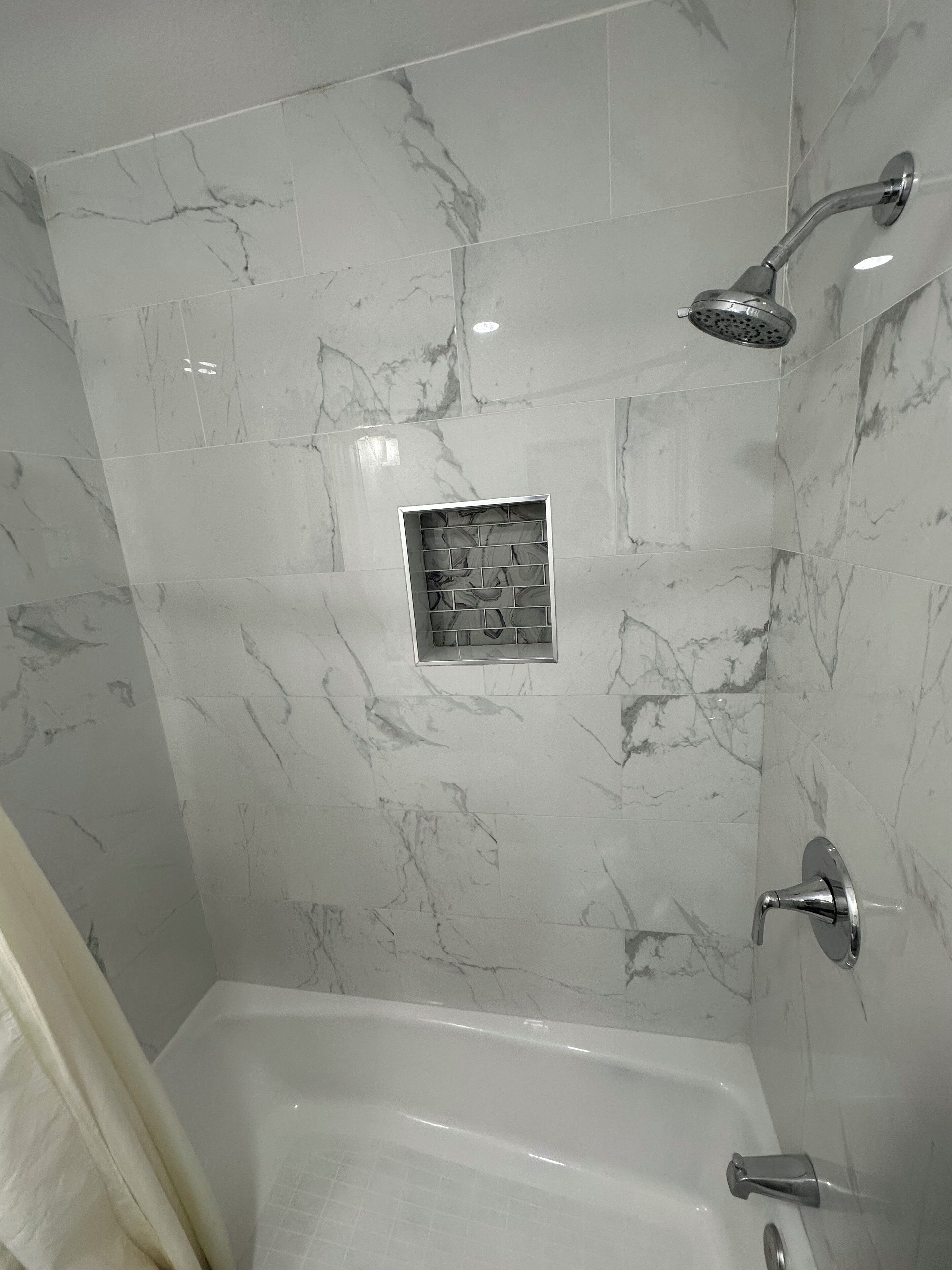 A bathroom with a shower, a bathtub, and a tiled wall with a marble pattern.