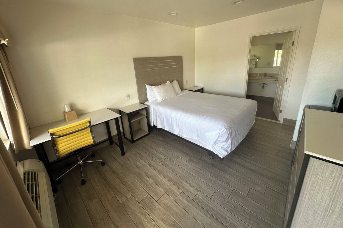 A hotel room with a bed, a desk, a chair, and a small table.