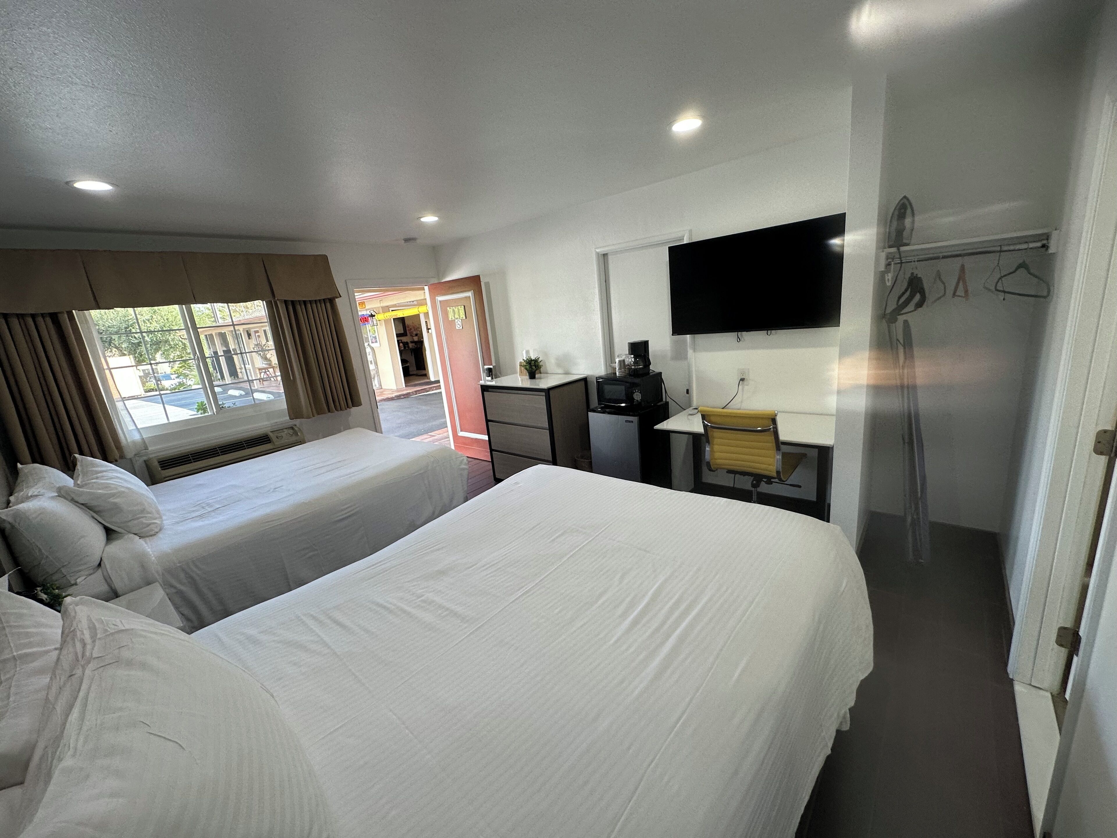 Quarto de hotel com duas camas, uma escrivaninha, televisão de tela plana, pequena cozinha e chuveiro.
