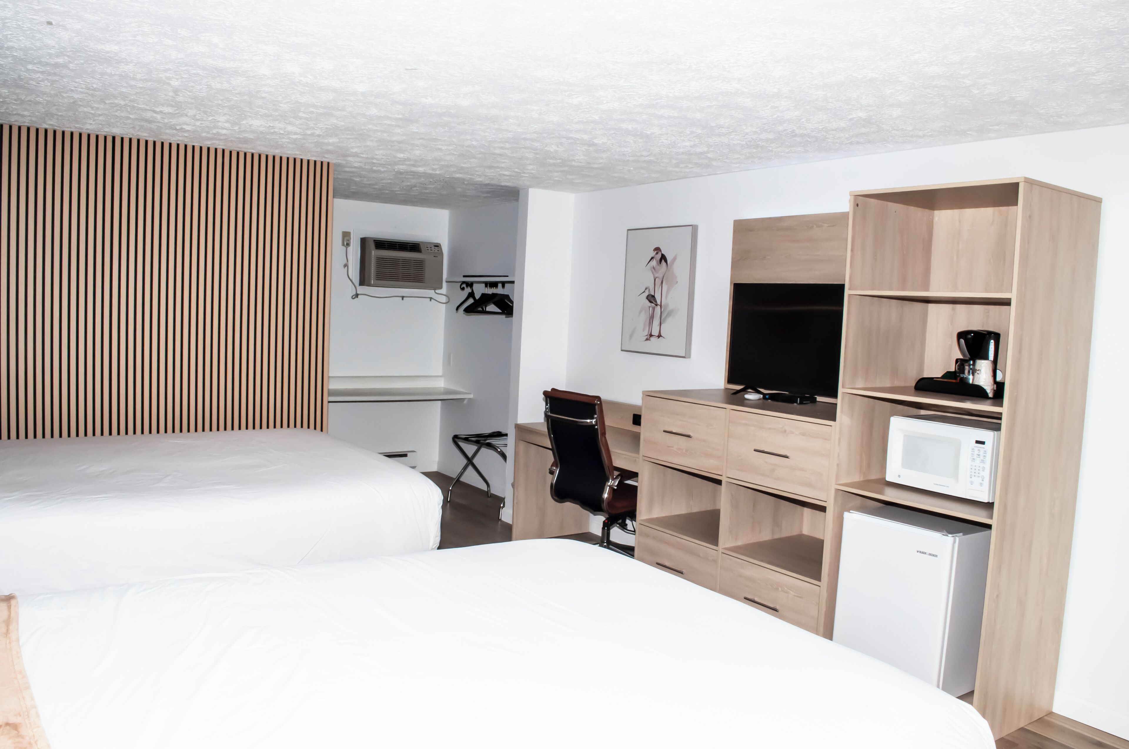 A modern hotel room with a bed, a desk, a chair, a TV, a microwave, and a small refrigerator.