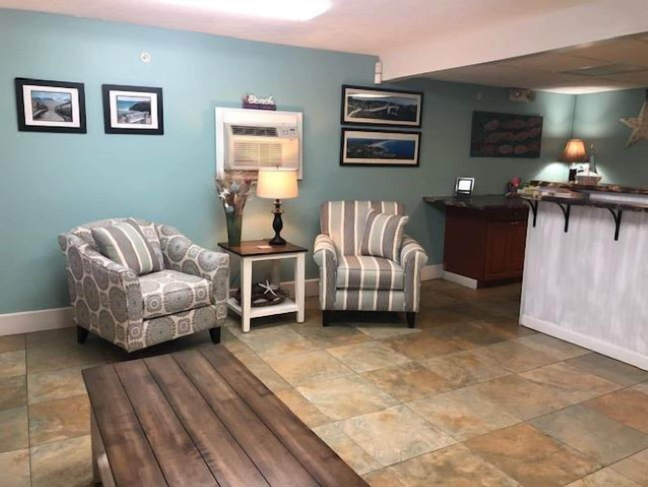 Un salon comprenant un fauteuil à motifs, un fauteuil à rayures, une table basse en bois et une petite table d’appoint avec une lampe.